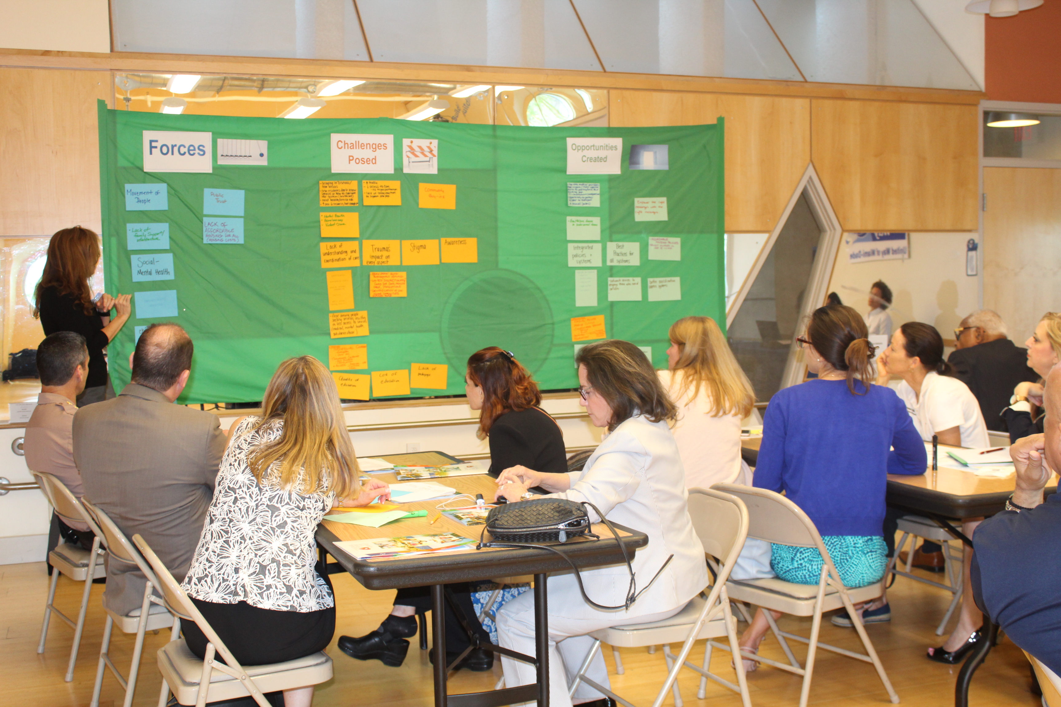 Classroom full of adults sitting and a teacher standing to the side of a green board full of index cards.