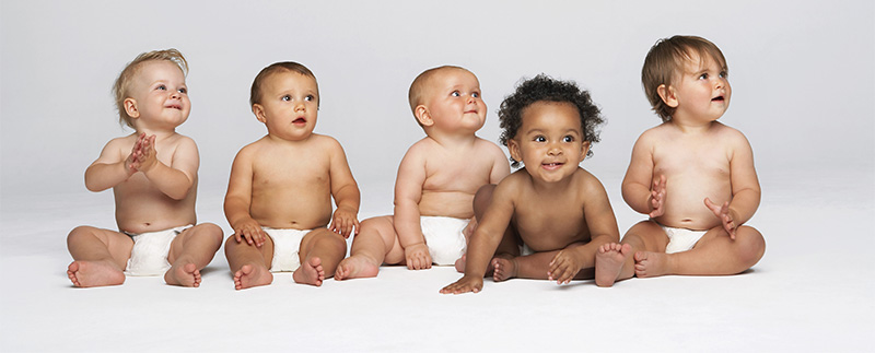 Five happy babies in diapers sitting in a horizontal line